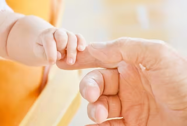 A close-up of a baby's hand holding onto an adult's finger.